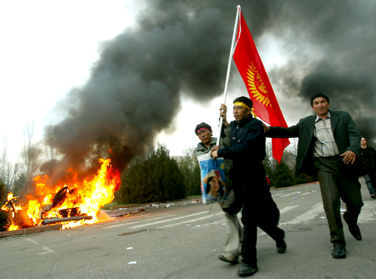 Kyrgyz opposition protesters walk past a burning car in Bishkek