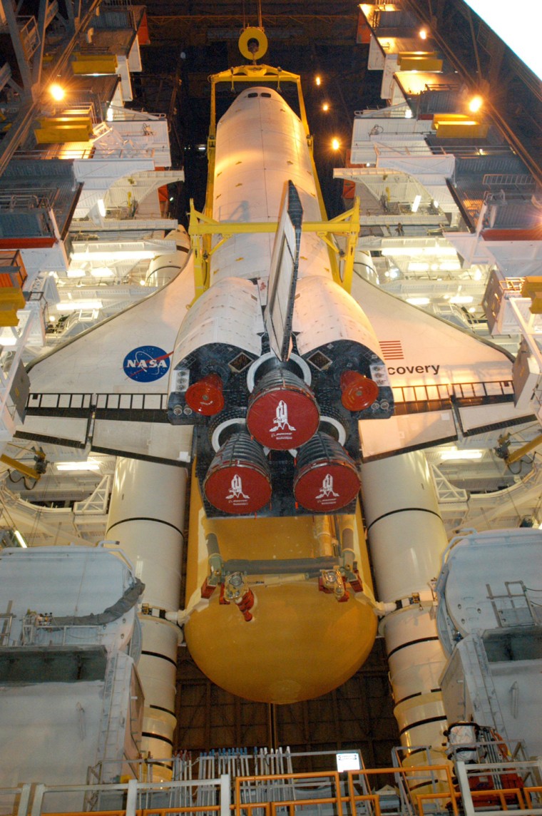 Inside NASA's Vehicle Assembly Building, the orbiter Discovery is lowered in front of its solid rocket boosters and external fuel tank for mating.