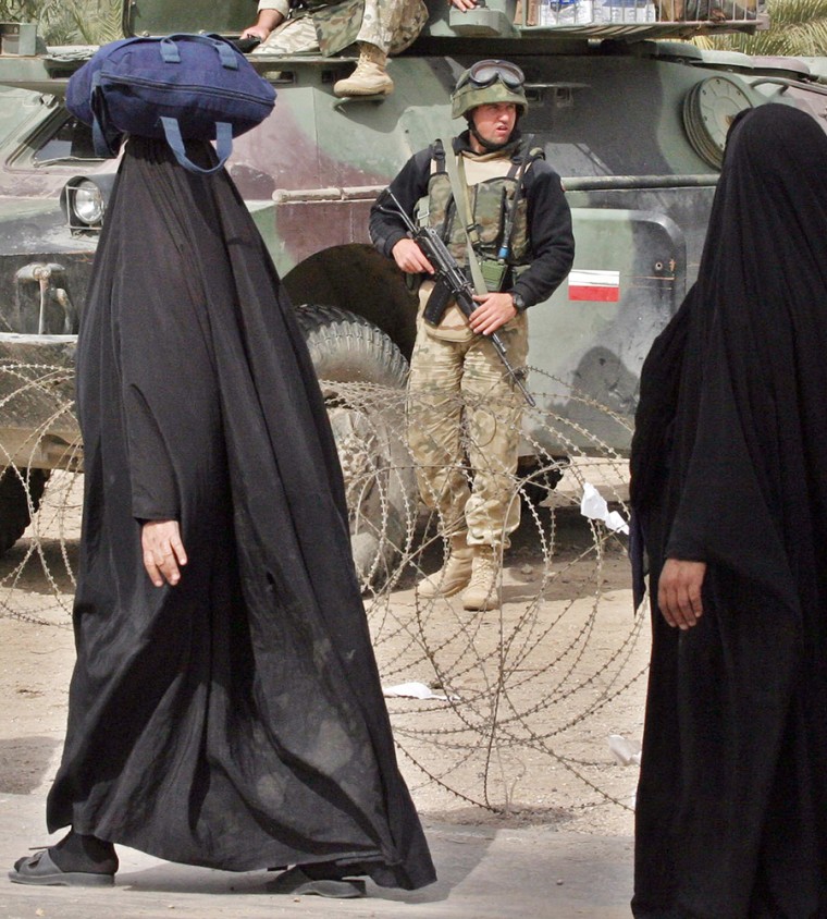 File photo of Iraqi women walking past a Polish soldier near Kerbala