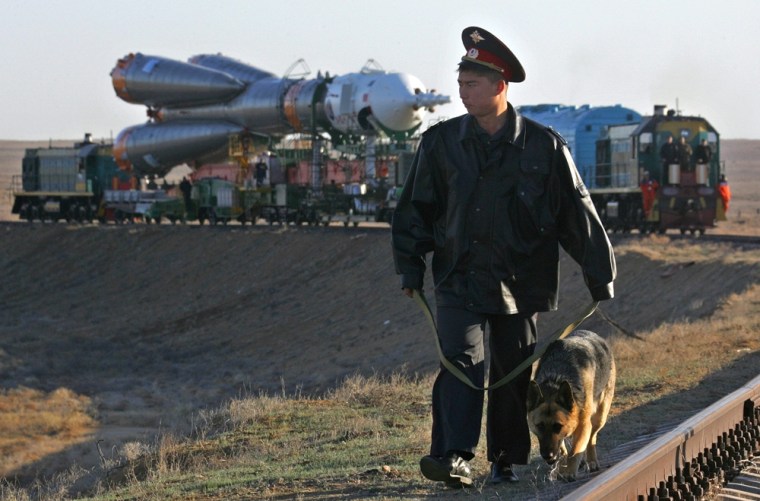 A police officer patrols with a dog as the Russian Soyuz rocket booster with the Soyuz TMA-6 spaceship is taken to a launch pad at the Baikonur cosmodrome in Kazakhstan on Wednesday.