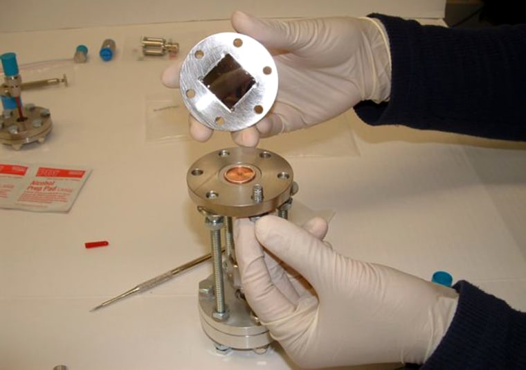 A researcher shows off the wafer test fixture that was used to test the new porous-silicon diode and its interactions with tritium gas. The diode is the dark wafer in the center of the top plate. 