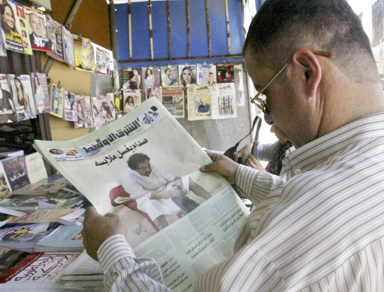 Iraqi man in Baghdad reads newspaper featuring pictures of Saddam Hussein in prison