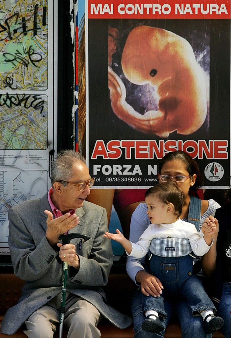 Passengers wait at a bus station in front of poster that reads \"Absence\", Rome