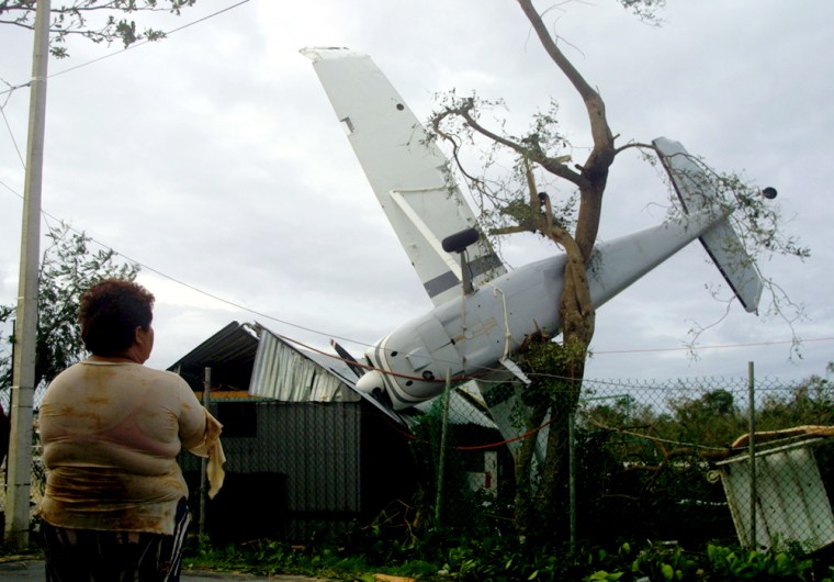 Mexican woman looks at aircraft which was flipped onto tree by Hurricane Emily's in Playa del Carmen, Mexico