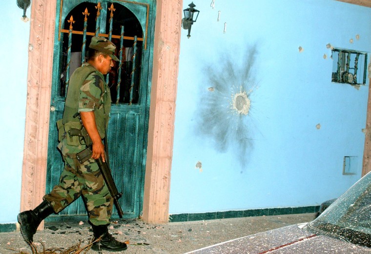 A Mexican soldier walks past a house riddled with bullet holes in Nuevo Laredo