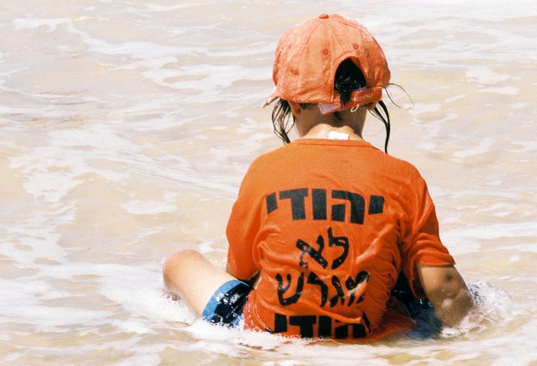 Caption:  A boy wearing an orange shirt, the color marking objection to the Israeli pullout from Gaza settlements, with the slogan, \"A Jew does not expell Jews,\"  a slogan widely used  by anti-pullout activists at the Neve Dekalim beach in Gush Katif. 

Credit: Miri Yehuda, NBC News