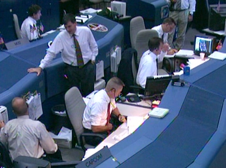 Capsule communicator Ken Ham, sitting at center in Houston's Mission Control and wearing a red tie, informs the Discovery crew that bad weather in Florida means they will aim to land instead in California’s Mojave Desert.