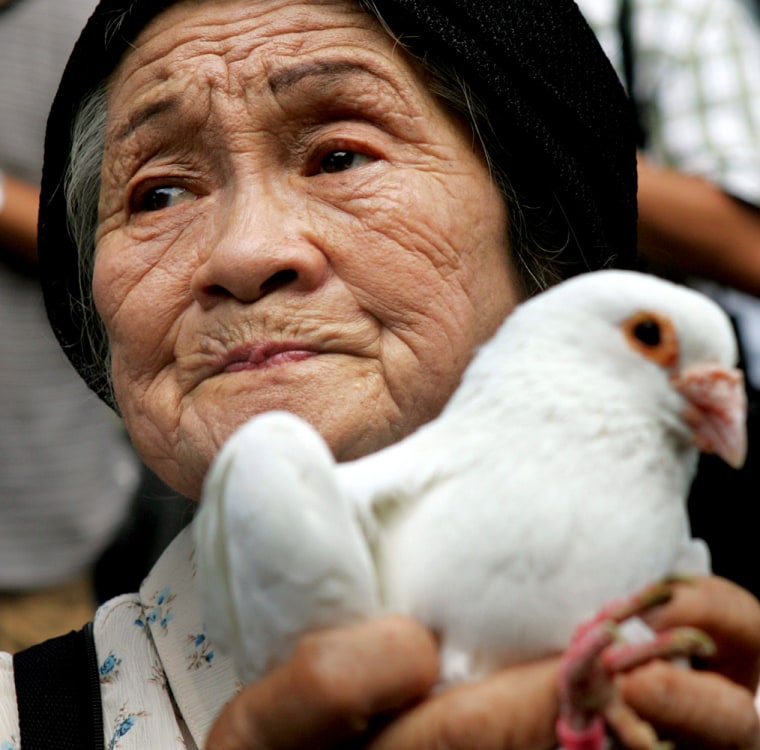 Elderly Japanese woman holds dove as she prays for souls of those killed in World War Two at Yasukuni Shrine in Tokyo
