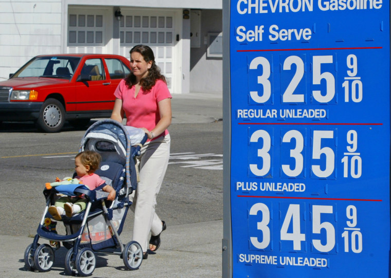 A woman pushes a baby in a stroller past a gasoline price sign in San Francisco
