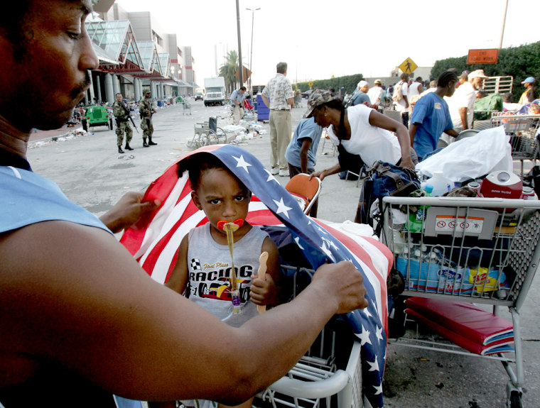 Jamaal Khalfani covers his daughter Violet Riles with an American flag to give her shade on Sunday as they wait outside the Convention Center in New Orleans.