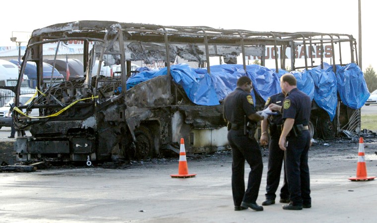 An emergency crew confers near the charred skeleton of a bus that caught fire and exploded early Friday on northbound Interstate 45 near Dallas.