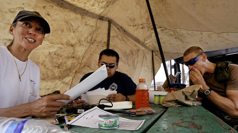 Lily Duke, left, a neighborhood resident and founder of a very large food, water and ice distribution center on Newton Street in New Orleans files through bills of  lading and inventory manifests while sitting at the sight's picnic table under a tent Thursday Nov, 10, 2005. Pierre, S.D., volunteer firefighter Sean Devine, center, helps Duke with her paperwork as Specialist Robert Everitt of Colorado's 1st Company 157 Field Artillery unit eats lunch.  (AP Photos/Stephan Savoia)