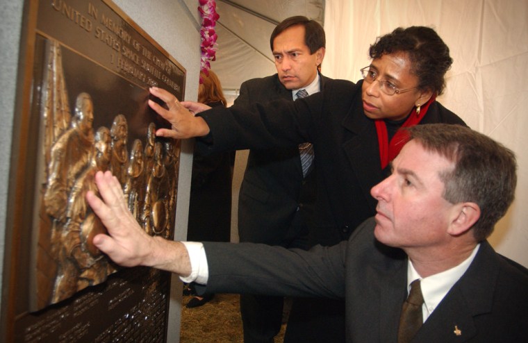 Sandy Anderson, the widow of fallen Columbia astronaut Michael Anderson, joins astronauts Carlos Noriega, left, and Stephen Robinson in touching a monument to the Columbia's crew at Arlington National Cemetery during its dedication in 2004.