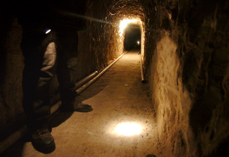 A Mexican police officer shines his flashlight in the tunnel.