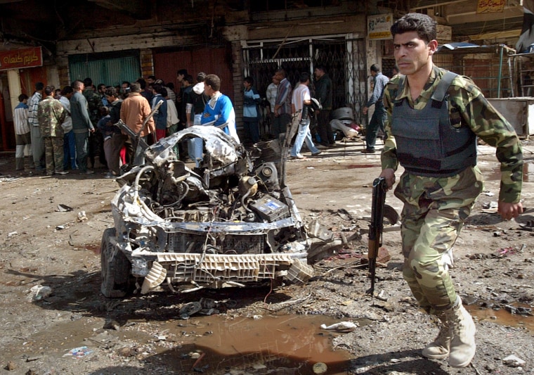 An Iraqi army soldier passes the wreckage of a car used in a bombing in Baghdad on Tuesday.