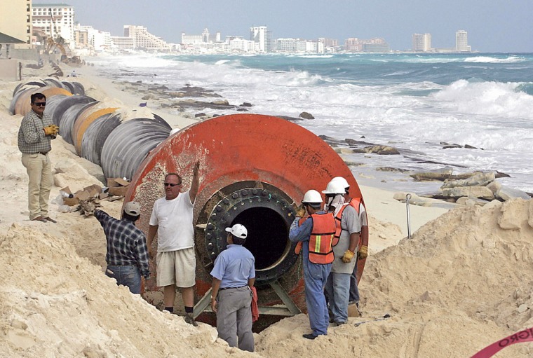 Workers install pipes used to drain sand