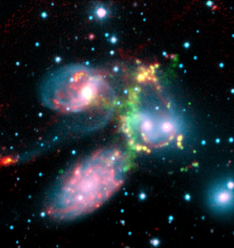 In this infrared composite image from the Spitzer Space Telescope, the pinkish blobs are galaxies, superimposed on a visible-light image of Stephan's Quintet. The greenish arc indicates a colossal shock wave generated as one galaxy falls toward another. The large spiral at lower left is a foreground galaxy that is not part of the cluster.
