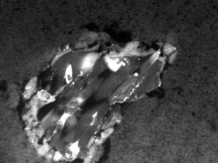 This image shows a comet particle about 2 micrometers across collected by Stardust. The particle is made up of the silicate mineral forsterite, also known as peridot in its gem form. It is surrounded by a thin rim of melted aerogel, the substance used to collect the samples.