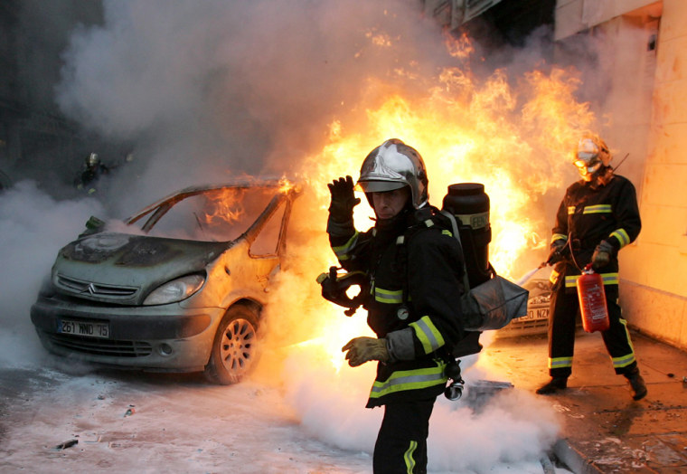 Firemen extinguish a burning car set on fire at the end of a student demonstration in Paris