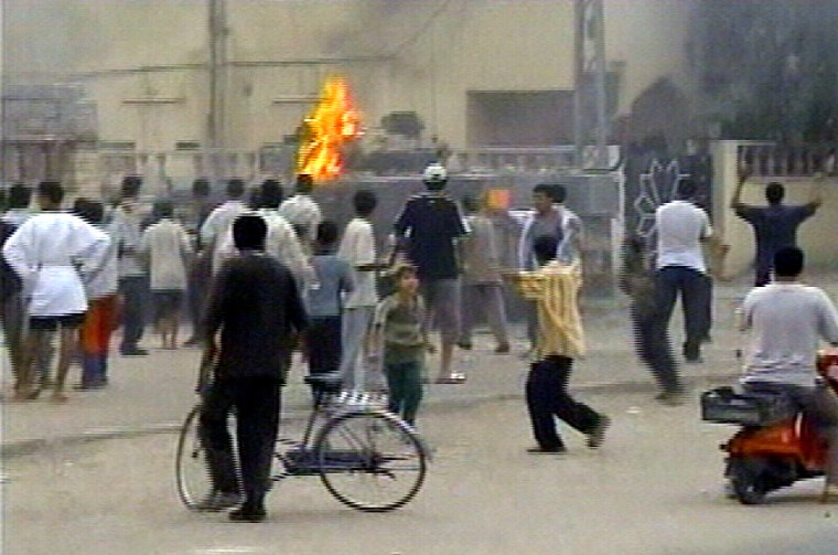 Crowds stand around and watch as others throw stones and Molotov cocktails at a British tank as it arrived on the scene where a British military helicopter crashed in Basra, Iraq, on Saturday in this image from TV.