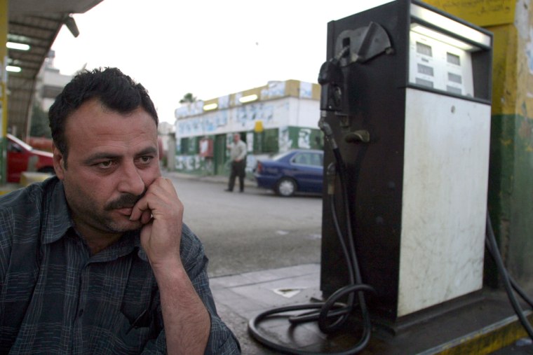 A Palestinian worker sits at a closed ga
