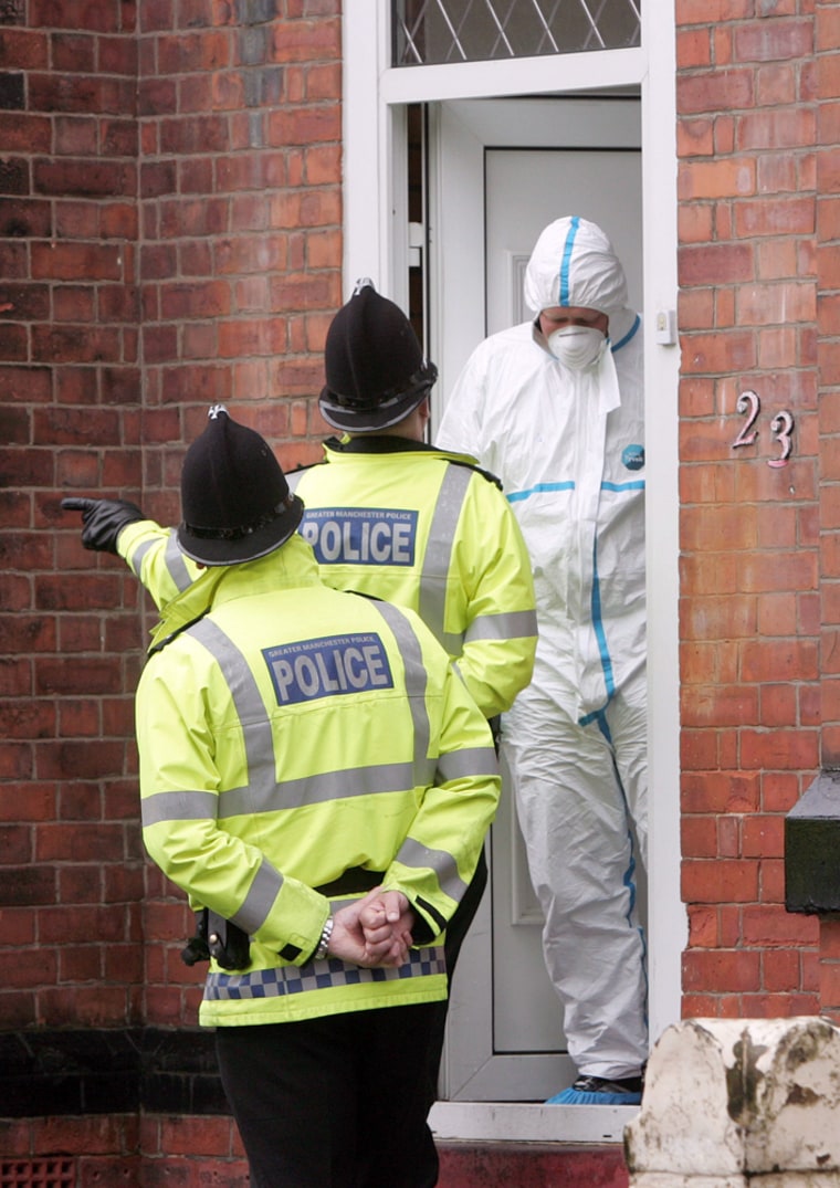 Police officers talk to a forensic officer as they stand outside a house in the Whalley Range area of Manchester