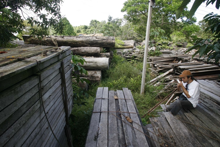 A ranger of IBAMA, the Brazilian national environmental agency, takes a cigarette break on top of confiscated timber at the agency's office in the northern city of Itaituba, Brazil, on Saturday, April 29, 2006. According to environmental groups, Brazil has only one forest ranger for every 650 square mile at its 278 federal preserves. (AP Photo/Andre Penner)
