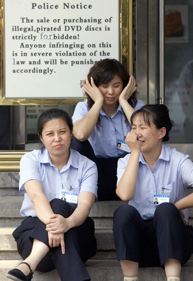 ** ADVANCE FOR FRIDAY JUNE 30 ** Chinese workers sit near a sign warning against the sale or purchase of pirated DVDs outside a shopping mall in Beijing, China, Tuesday, June 27, 2006. The war against rampant Chinese piracy of counterfeit movies, drugs and other products is moving from the back alleys and sidewalks into boardrooms and laboratories, as companies hunt new ways to fight back. (AP Photo/Ng Han Guan)