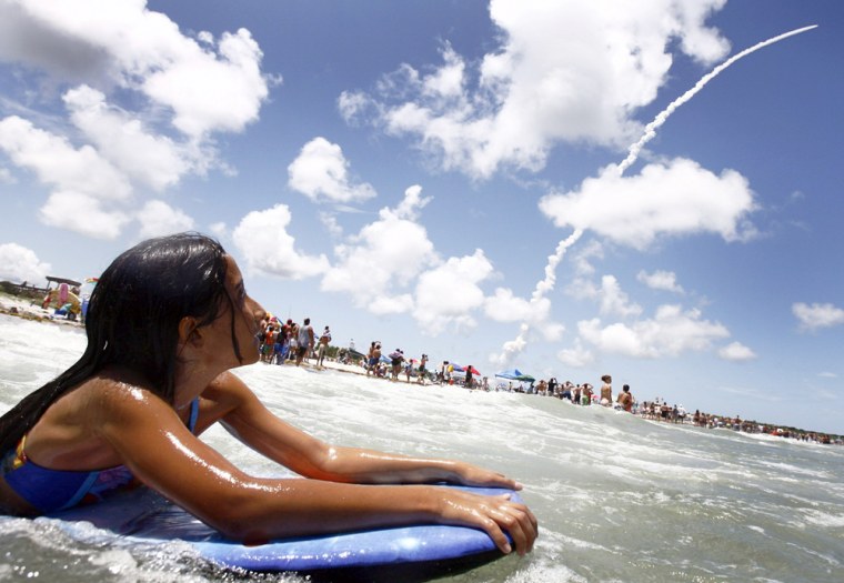 Girl takes a wave as space shuttle Discovery lifts off from the Kennedy Space Center in Cape Canaveral