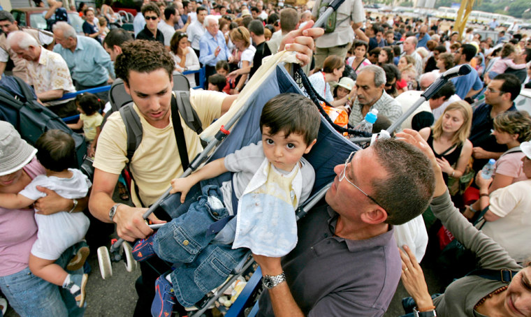 A French toddler is carried over a fence by relatives as they wait Monday with hundreds of other French citizens near their embassy in Beirut to be evacuated from Lebanon.