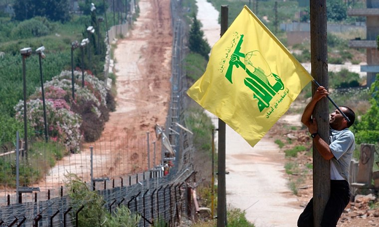 A Lebanese supporter of Hezbollah waves the group's flag as he climbs up an electricity pole in front of the Lebanese-Israeli border fence, in southern Lebanon in May.