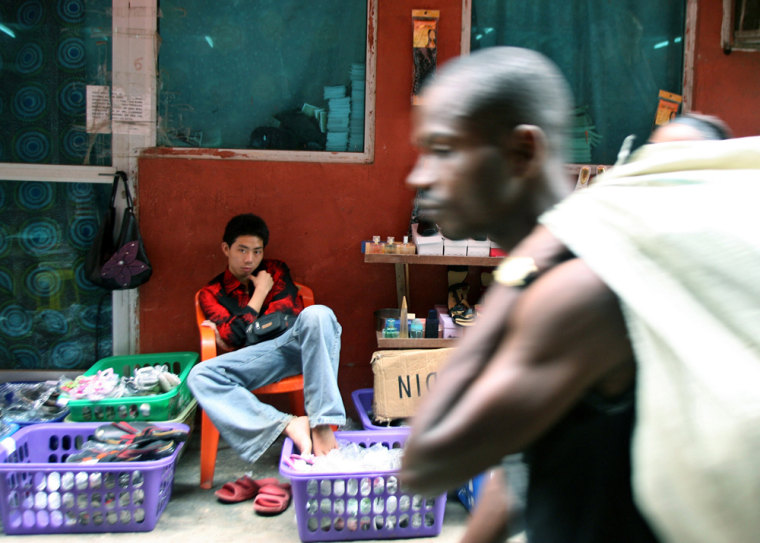 An unidentified man walks past a Chinese trader sitting in front of his shop at the China town trading compound in Lagos, Nigeria.  