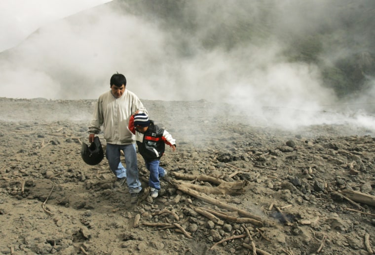 An Ecuadorian man and his son walk over cooled lava from the Tungurahua volcano in Banos, Ecuador, on Thursday.