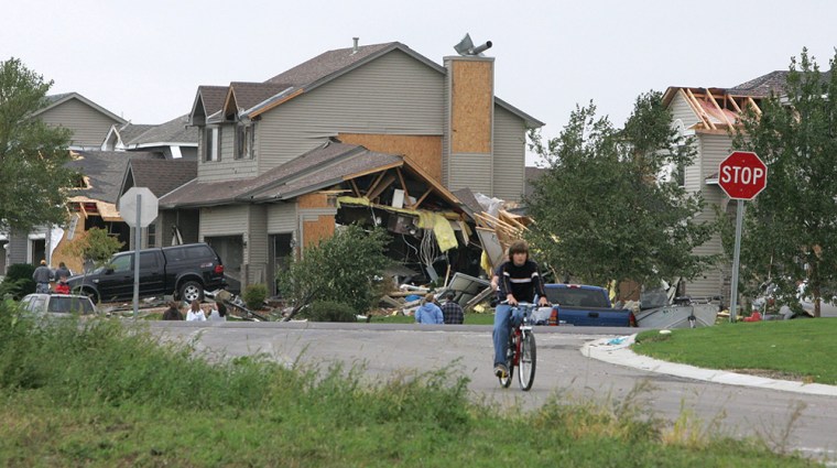 A boy rides his bike Sunday morning near damaged homes in Rogers, Minn., after high winds swept through the town Saturday night.