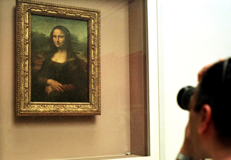 A visitor to the Louvre in Paris takes a photograph of Leonardo da Vinci's "Mona Lisa," which is mounted behind protective glass.