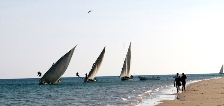Fishermen struggle to control traditional sailing dhows in strong winds as two tourists walk on the beach in Lamu, Kenya, Feb. 25. 