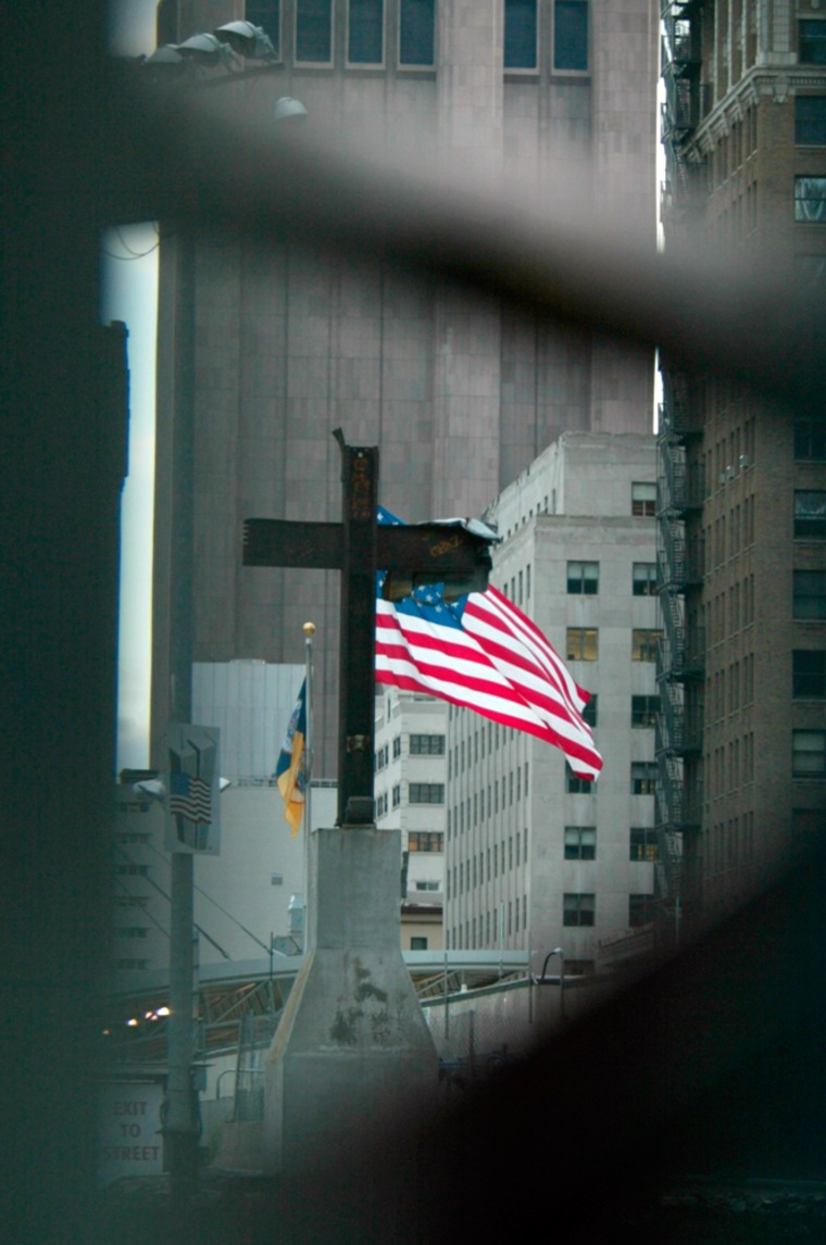 As viewed through a fence, a giant American flag flies in the wind behind a steel beam cross at ground zero of the World Trade Center site in New York, Thursday Oct. 5.