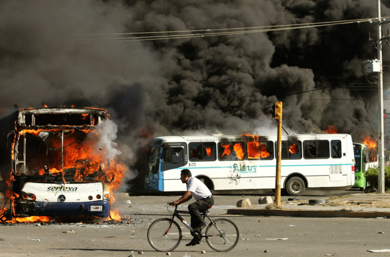 A man cycles past burning buses during a federal forces operation in Oaxaca City