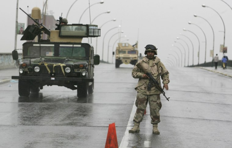 Soldier stands guard as US armoured vehicles patrol a road during the second day of curfew in Baghdad
