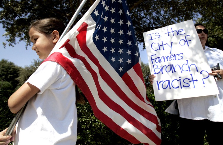 Natalie Villafranca holds an American flag as her mother, Elizabeth Villafranca, holds a sign in front of city hall in Farmers Branch, Texas, on Saturday.