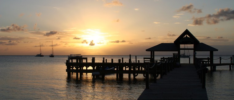 The sun sets with Luna Beach Resorts dock in the foreground, on the Honduran island of Roatan.