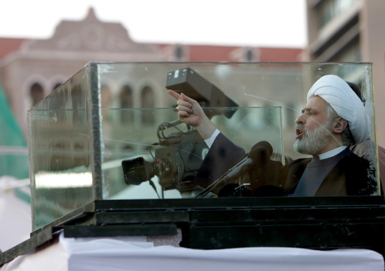Sheik Naim Kassem, the deputy of Hezbollah leader Sheik Hassan Nasrallah, speaks from behind a glass screen to the crowed in front of the Lebanese government house, seen in the background, during the tenth day of an open-ended protest to force the resignation of Lebanese Prime Minister Fuad Saniora, in Beirut, Lebanon, Sunday Dec. 10, 2006. Kassem called on the government to resign and said the opposition was willing to stay on the streets for months to achieve the goal. He said the powerful show of masses should send a message to the United States and other countries which support Saniora. (AP Photo/Hussein Malla)