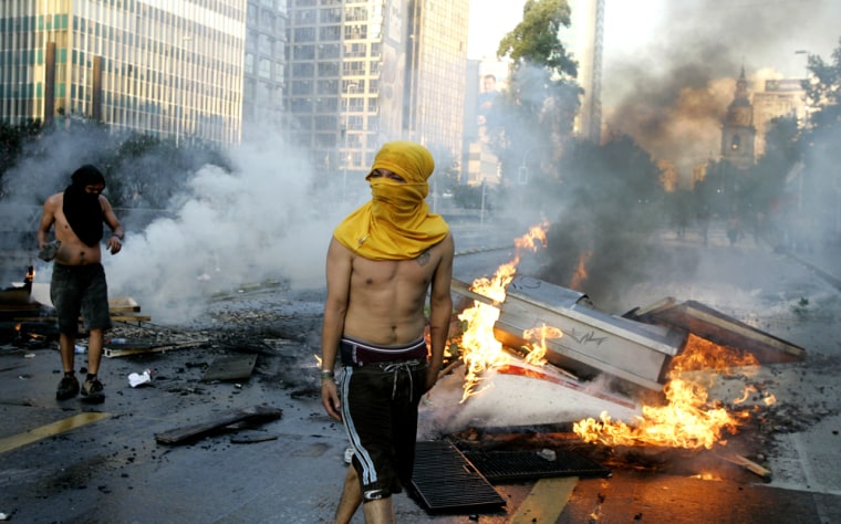 Opponents of former Gen. Augusto Pinochet stand next to burning barricades in downtown Santiago on Chile on Sunday.
