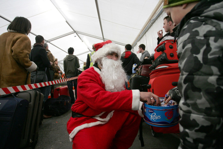 An airport staff member dressed in a Santa outfit hands out sweets to passengers waiting in a tent erected outside terminal four of Heathrow airport, Friday, Dec. 22. 