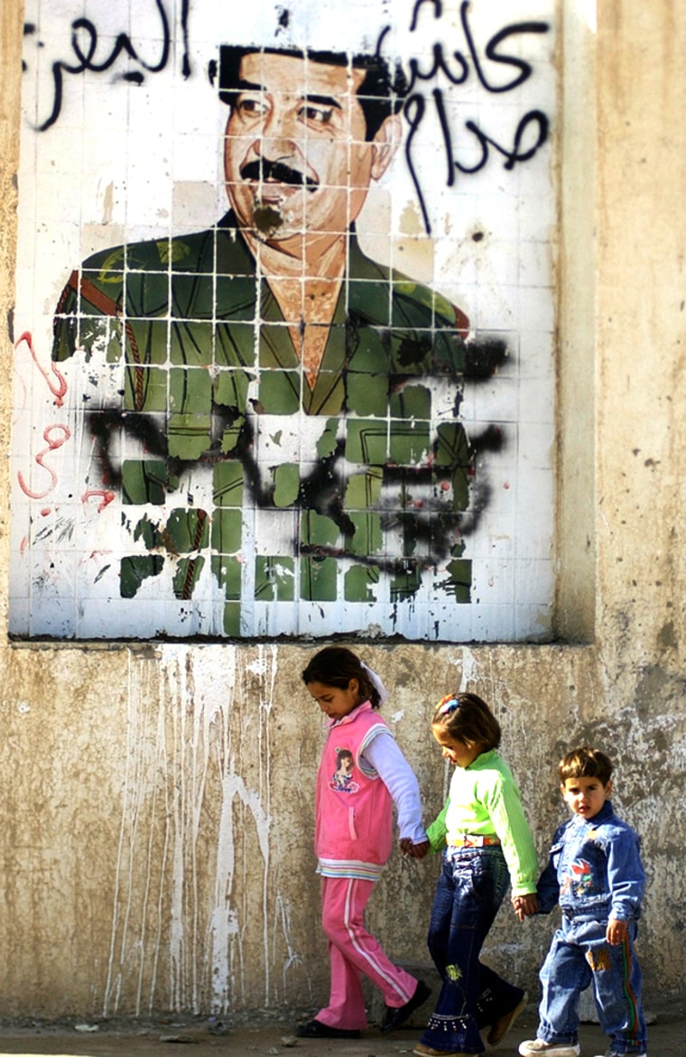 Iraqi children pass by a vandalized mural of the former Iraqi dictator Saddam Hussein in Tikrit on Thursday.