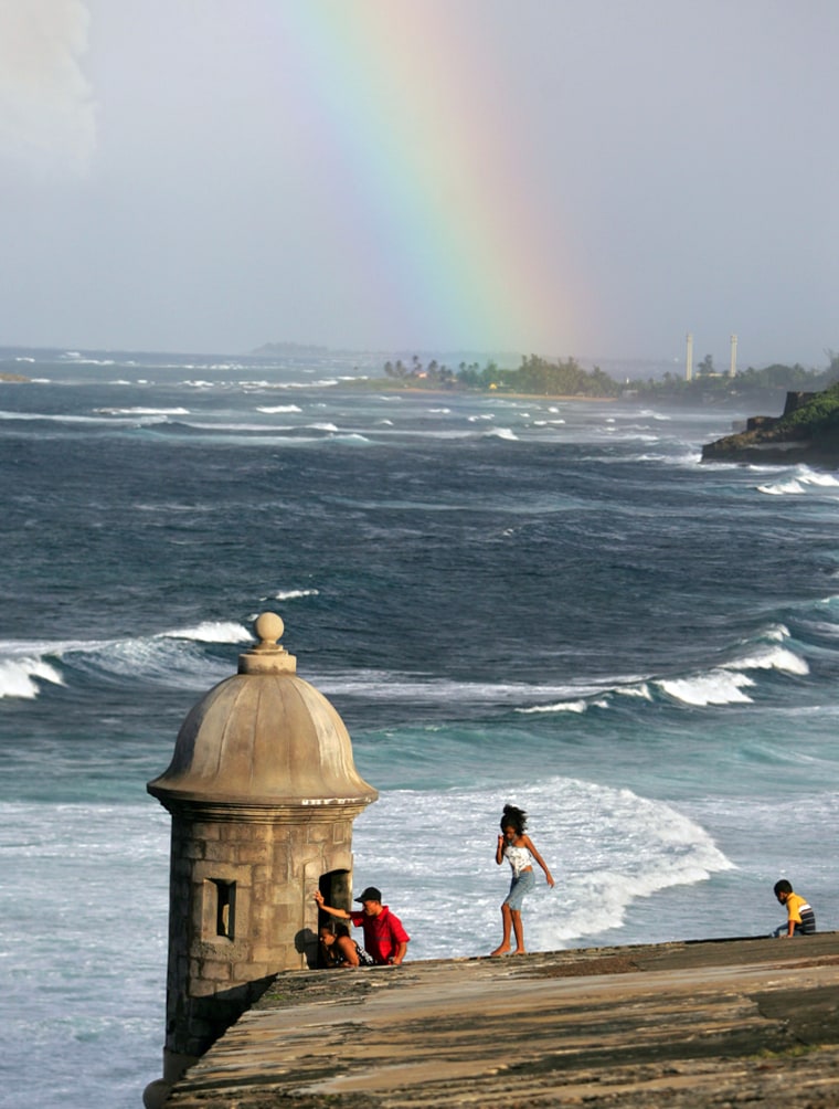 A family explores the seaside walls of El Morro Fort, as a passing rain shower creates a rainbow as seen from Old San Juan, Puerto Rico.