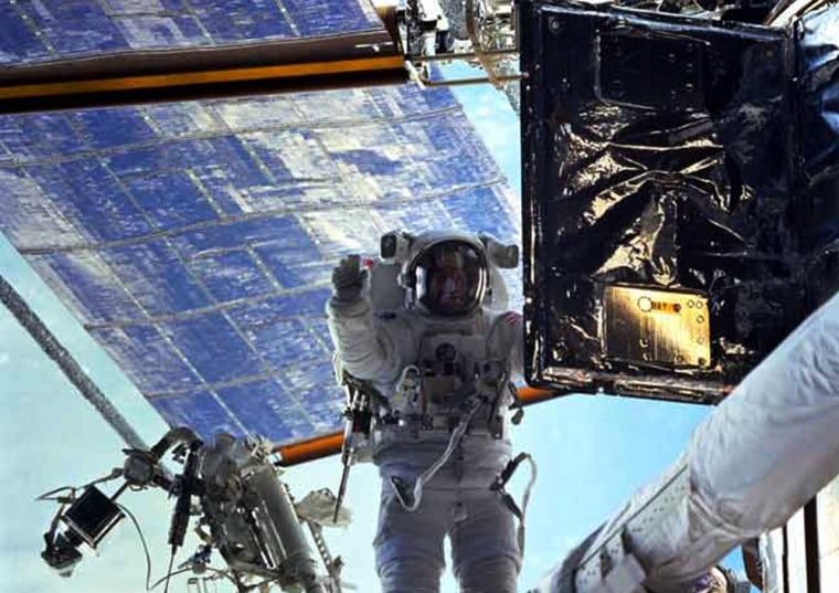 Astronaut John Grunsfeld stand on a foot restraint and prepares to replace a radio transmitter on the Hubble Space Telescope.