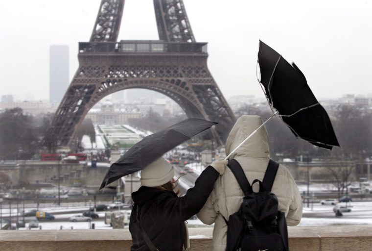 Tourists fight against gust of wind as they stand near Eiffel Tower in Paris