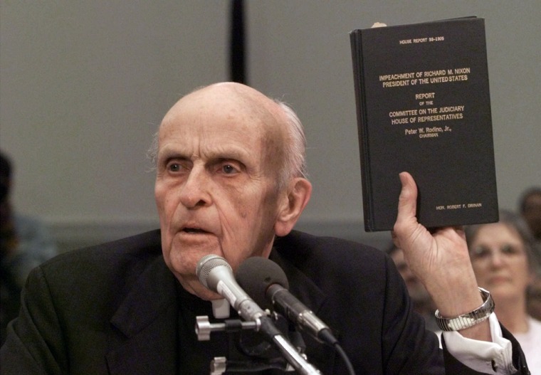Former Massachusetts Rep. Robert Drinan holds up a copy of the 1974 impeachment report of President Nixon while testifying on Capitol Hill on Dec. 8, 1998
