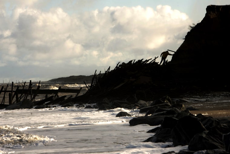 A man walks over debris from previous barriers and collapsed contructions that had destroyed due to errosion  at the northeastern coastal village of Happisburgh, in Norfolk, England, Wednesday Jan. 24, 2007. Many houses of the village are in danger as the offshore barrier that once protected the sand and clay bluffs below has broken apart, and England's government has decided not to replace it. Global warming's expected increase in sea levels and storm surges mean that some vulnerable coastal areas just aren't worth defending any more. Property values of the village's seaside homes have plummeted, and the owners will receive no compensation from the government for their lost homes, only the offer of public housing. (AP Photo/Lefteris Pitarakis)